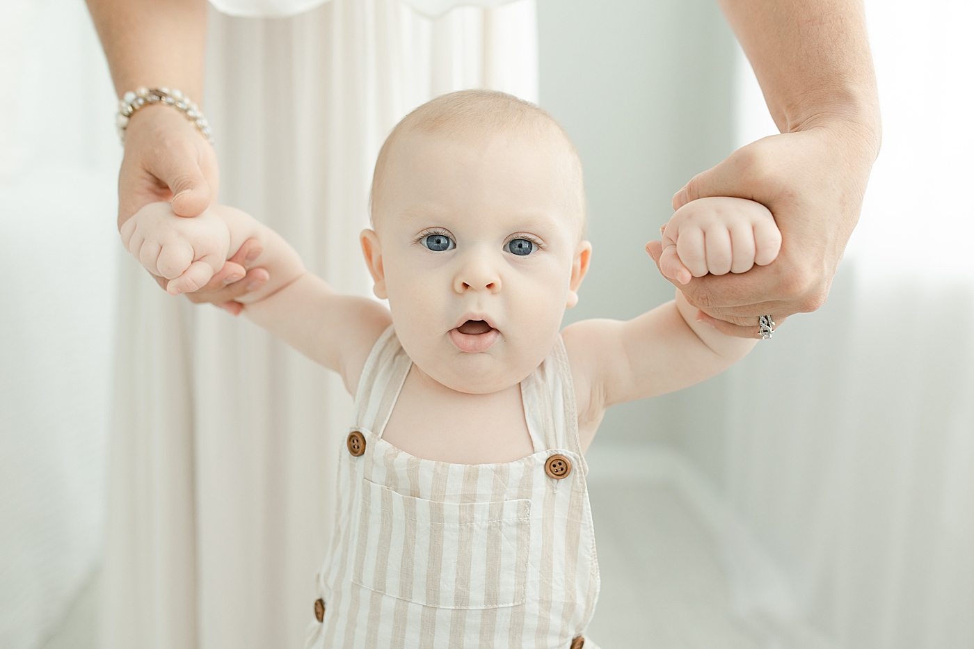 Baby boy holding mom's hands while standing | Photo by Little Sunshine Photography