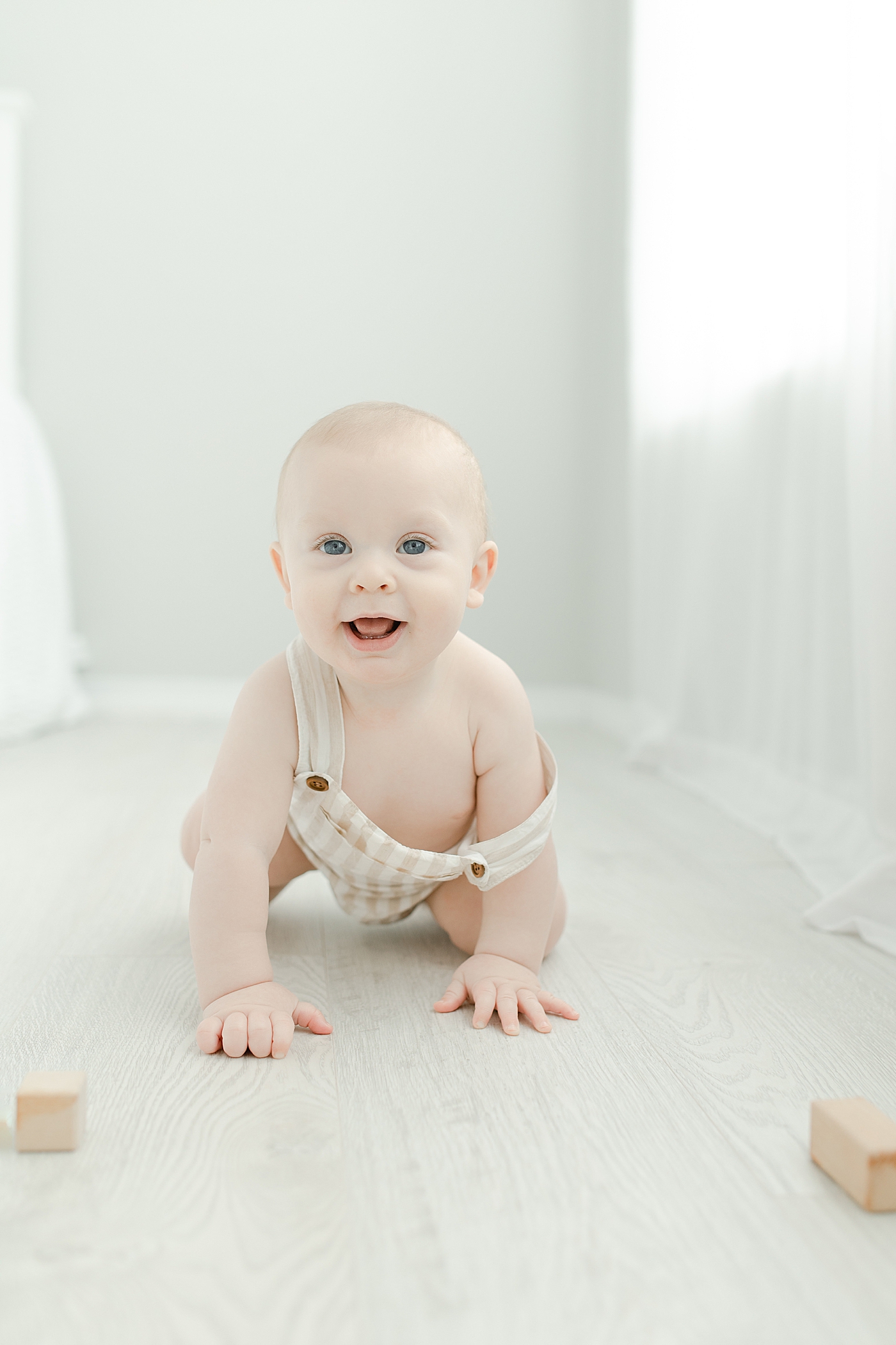 Baby boy in striped overalls smiling while crawling | Photo by Hattiesburg Baby Photographer Little Sunshine Photography