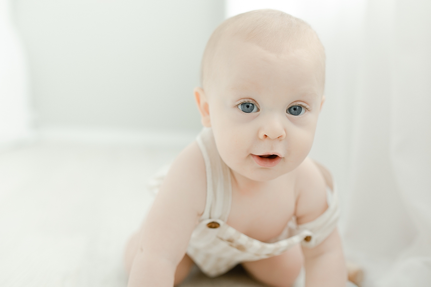 Baby boy with blue eyes in striped overalls | Photo by Little Sunshine Photography