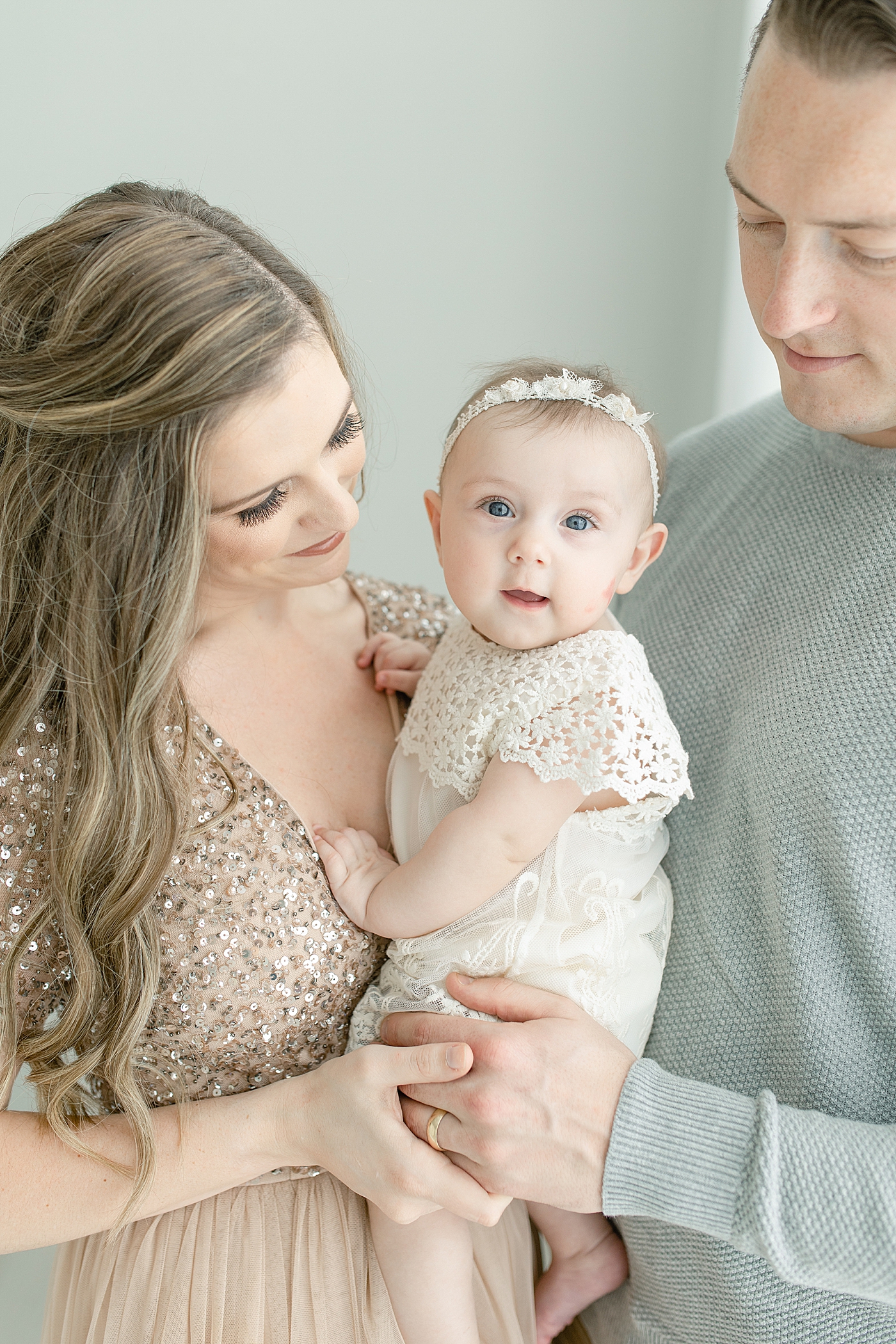 Blue eyed baby girl in white dress with mom and dad for six month milestone session | Photo by Little Sunshine Photography