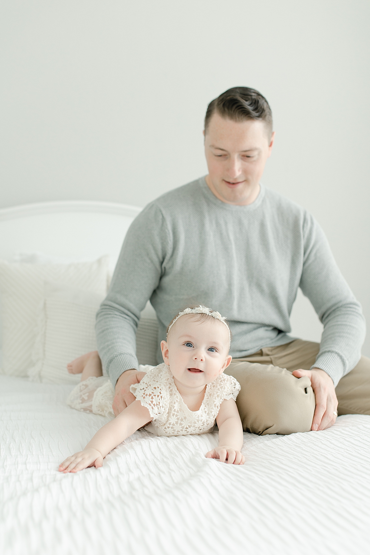 Dad sitting with his baby girl on a white bed | Photo by Little Sunshine Photography