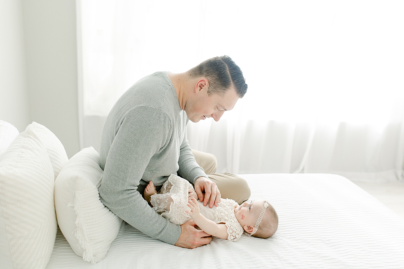 Dad sitting with his baby girl on a bed | Photo by Little Sunshine Photography