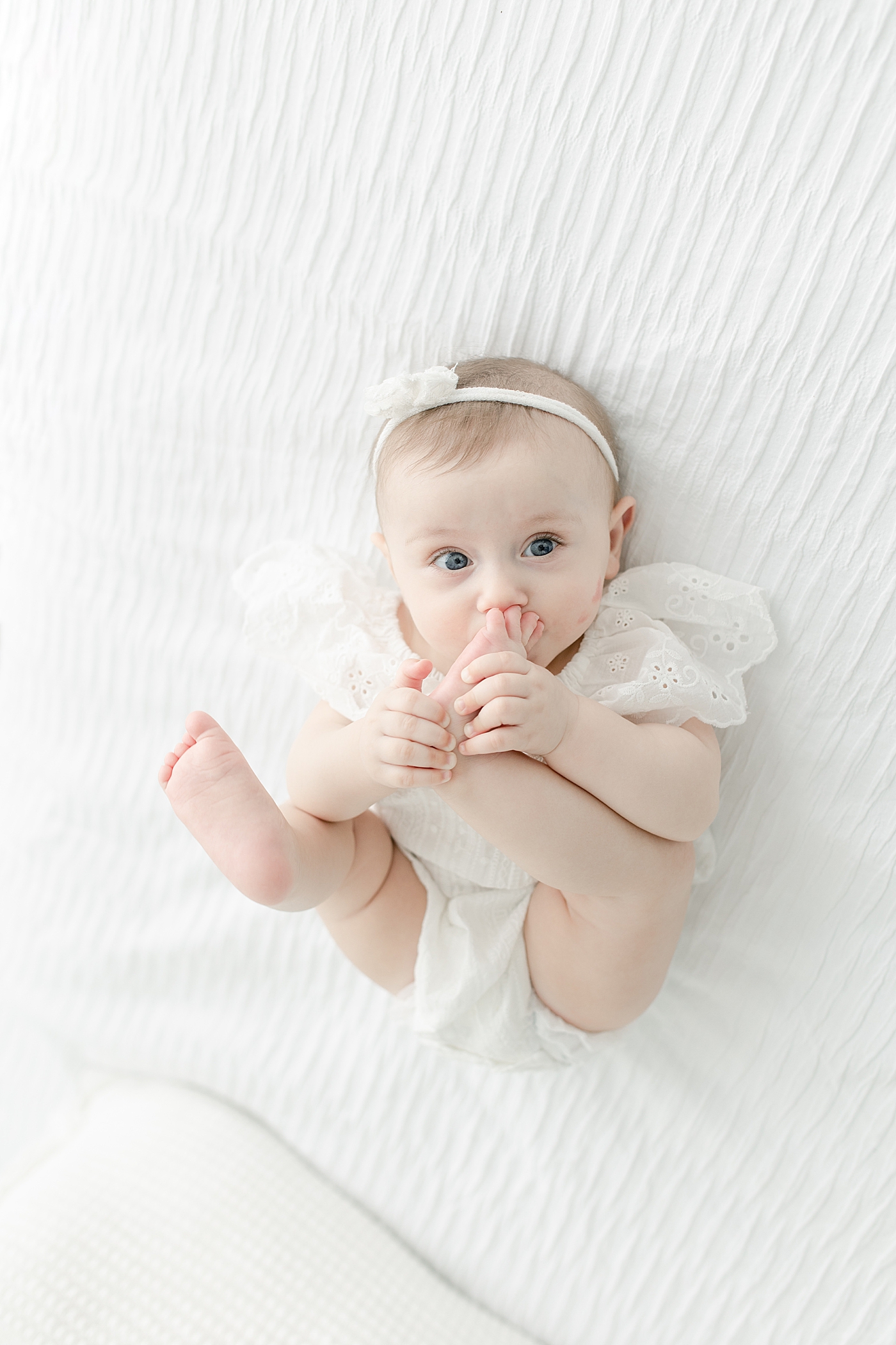 Baby girl in white holding her feet at six month milestone session | Photo by Pass Christian baby photographer Little Sunshine Photography