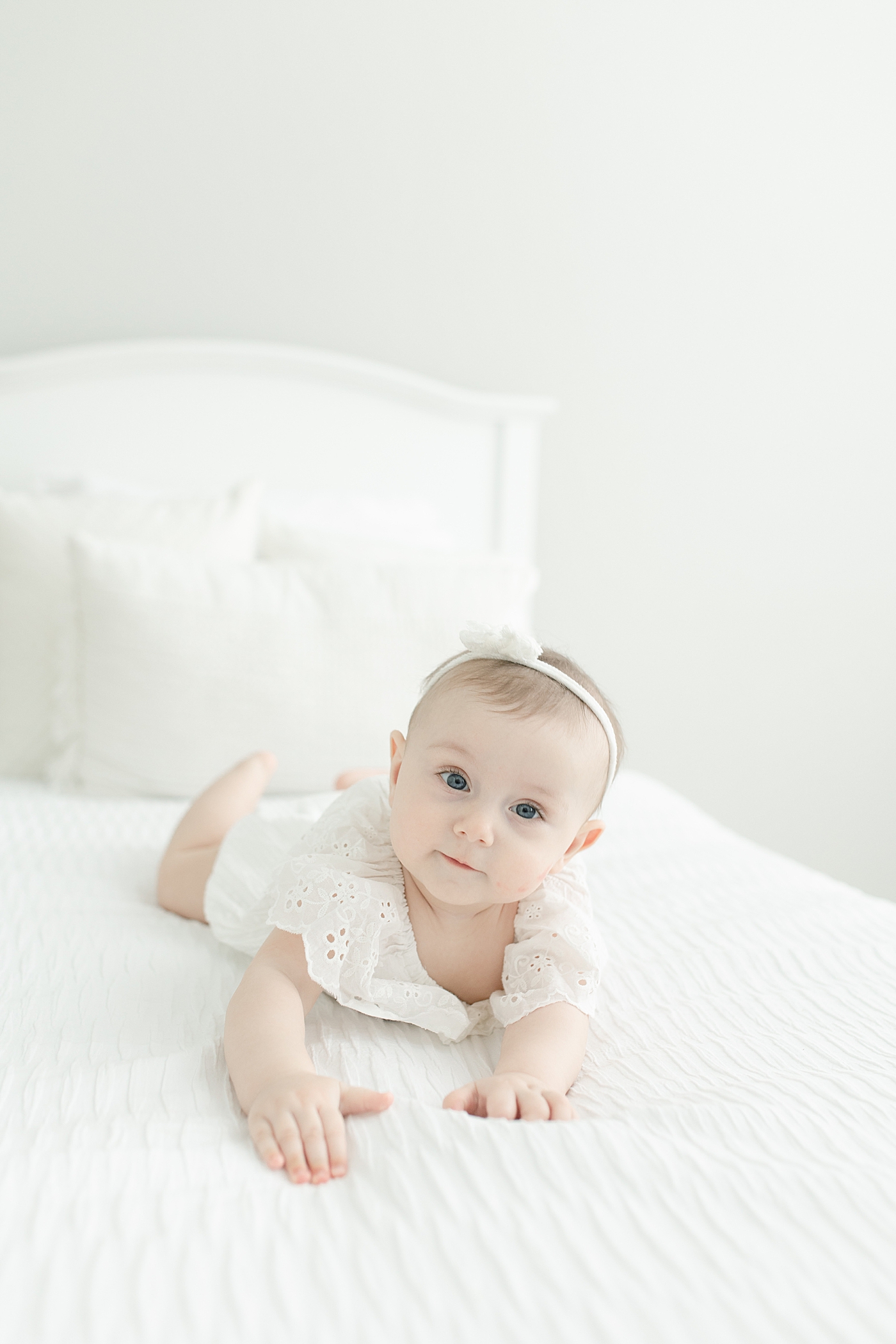 Baby girl in white dress and headband laying on her belly at six month milestone session | Photo by Pass Christian baby photographer Little Sunshine Photography