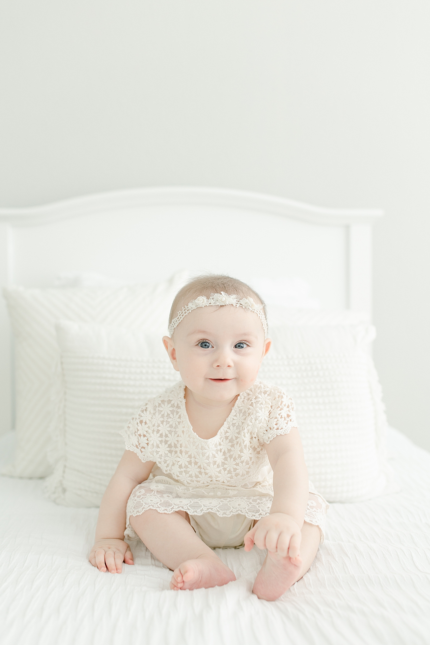 Blue eyed baby girl in white dress sitting on a bed | Photo by Pass Christian baby photographer Little Sunshine Photography